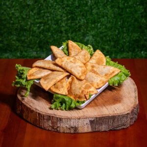 A plate of golden crispy samosas on lettuce, placed on a rustic wooden platter.